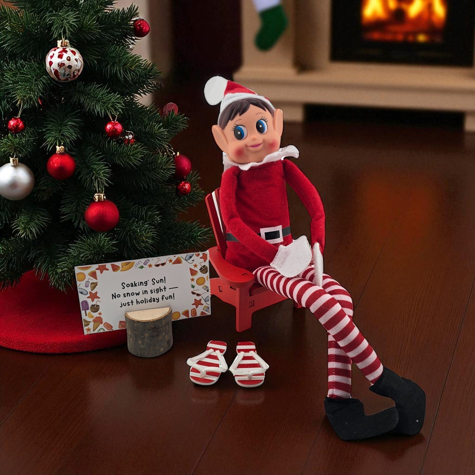 Christmas elf doll sitting on a miniature red beach lounge chair prop by a tree from the 24 day elf kit.