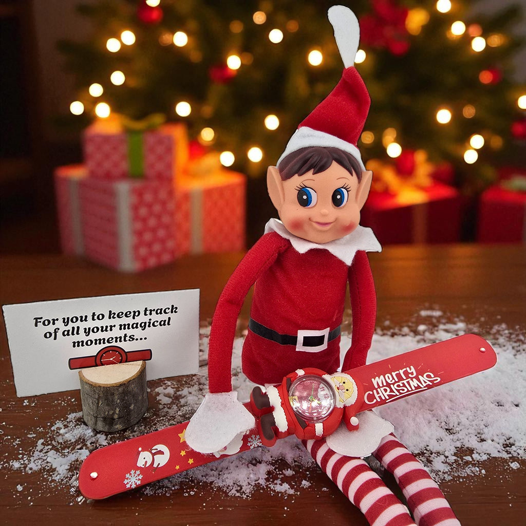 Christmas elf doll sitting in faux snow next to a red Merry Christmas slap wrist watch from the 24 day elf kit.